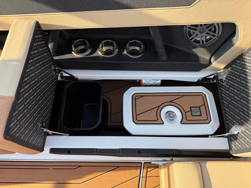 Slide: The Image of 2025 Nautique Super Air GS22 boat storage compartment with cup holders and speaker. - 53