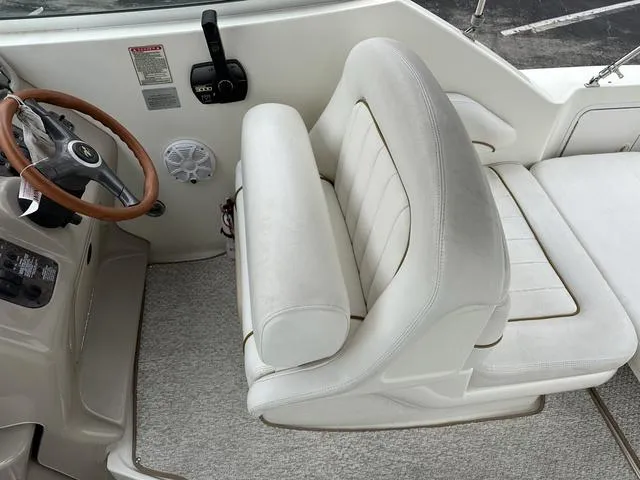 Slide: The Image of 1999 Sea Ray 270 Sundancer helm with white cushioned captain's seat and wooden steering wheel. - 11