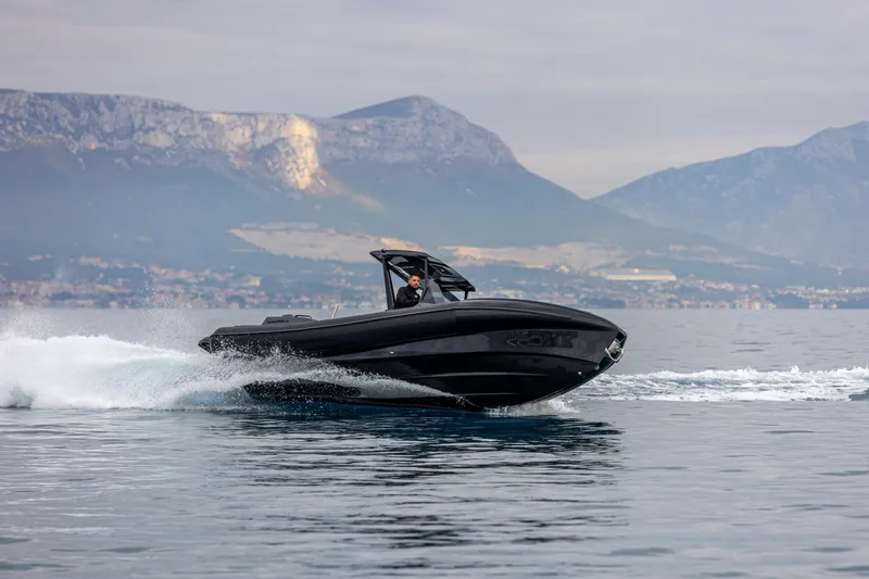 Slide: The Image of A sleek 2026 SuperRib Open 27 boat cruising on calm waters with mountainous backdrop. - 13