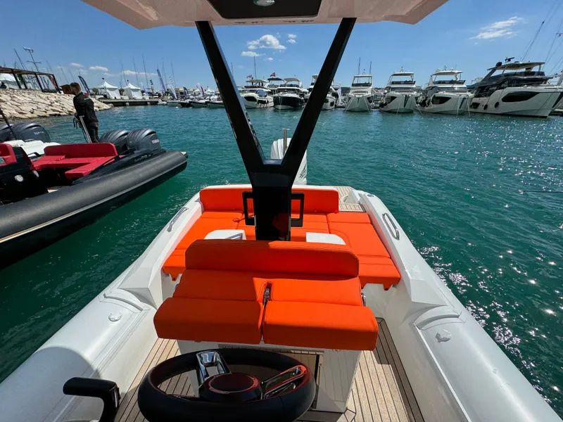 Slide: The Image of 2025 SuperRib Open 27 boat with orange seating, docked at a marina with yachts. - 18