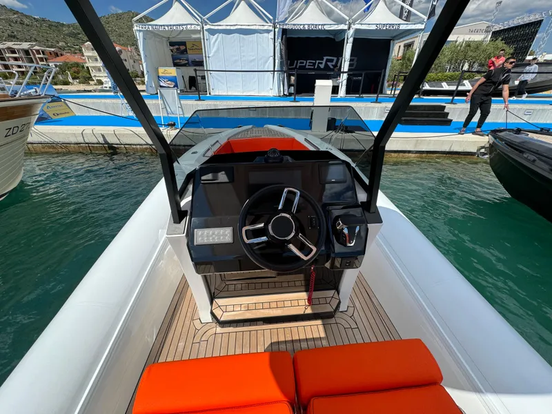 Slide: The Image of 2025 SuperRib Open 27 boat dashboard with steering wheel and orange seating at marina. - 23