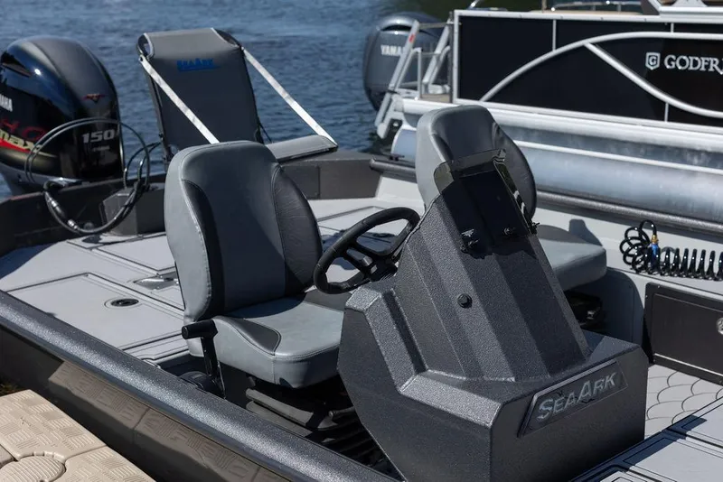 Slide: The Image of 2024 SeaArk FLEX21 boat interior with steering console and seating, docked by the water. - 7