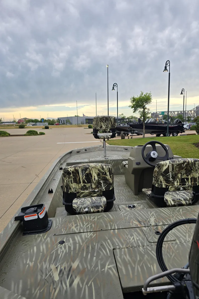 Slide: The Image of 2024 Tracker Grizzly 1754 SC boat with camo seats and steering wheel, parked outdoors. - 2