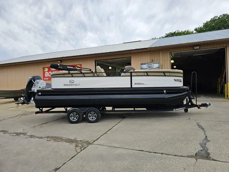 The Image of 2024 Regency 230 DL3 pontoon boat on a trailer outside a warehouse. - 0