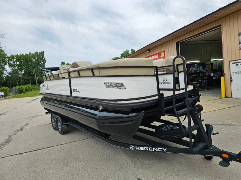 Slide: The Image of 2024 Regency 230 DL3 pontoon boat on a trailer outside a garage. - 1