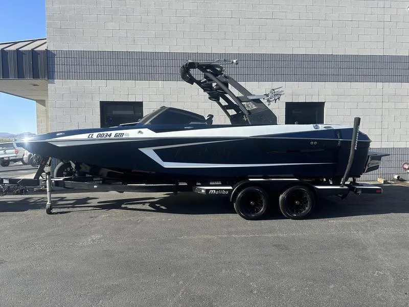 Slide: The Image of 2024 Malibu 23 MXZ boat on a trailer, parked beside a building. - 0