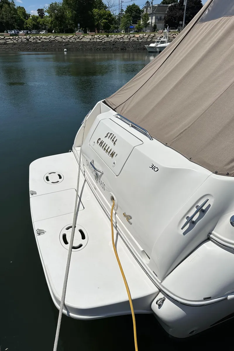 Slide: The Image of 1999 Sea Ray 310 Sundancer docked, rear view with cover, on calm water. - 7