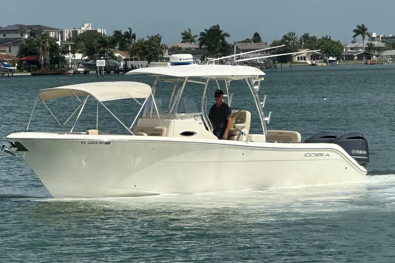 Slide: The Image of 2016 Cobia 296CC boat cruising on water with coastal homes in the background. - 2