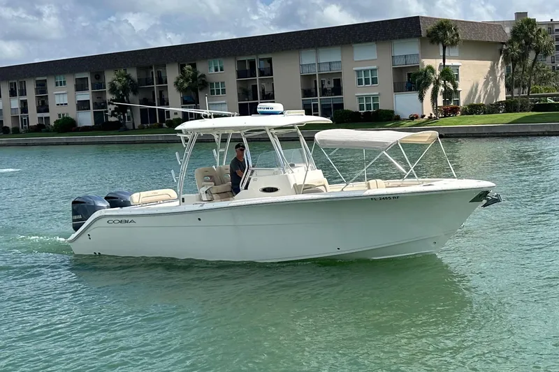 Slide: The Image of 2016 Cobia 296CC boat cruising on a calm waterway near residential buildings. - 4