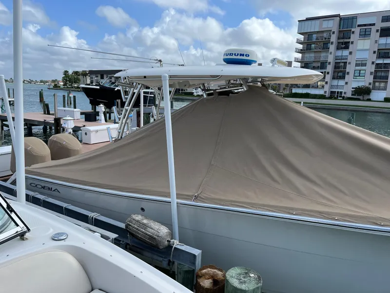 Slide: The Image of 2016 Cobia 296CC boat docked with cover, waterfront view, and nearby buildings. - 6