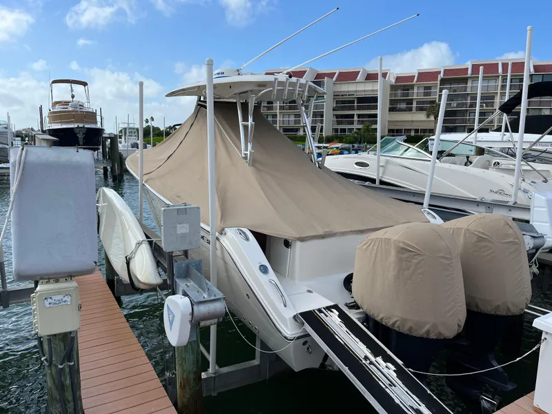 Slide: The Image of 2016 Cobia 296CC boat docked with protective covers, marina background. - 8