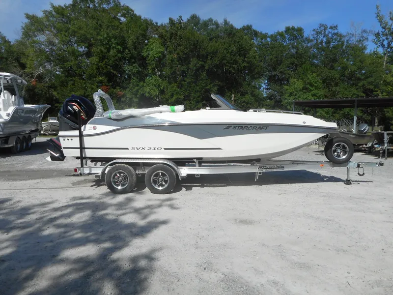 Slide: The Image of 2024 Starcraft SVX 210 OB DC boat on a trailer in an outdoor setting. - 0