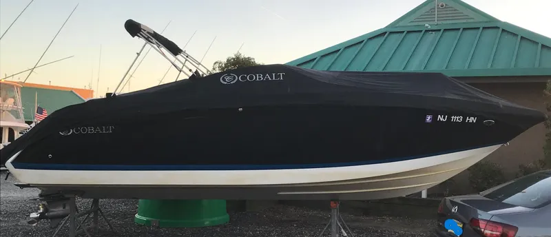 Slide: The Image of 2013 Cobalt 26SD boat covered, parked outdoors near a green-roofed building. - 18