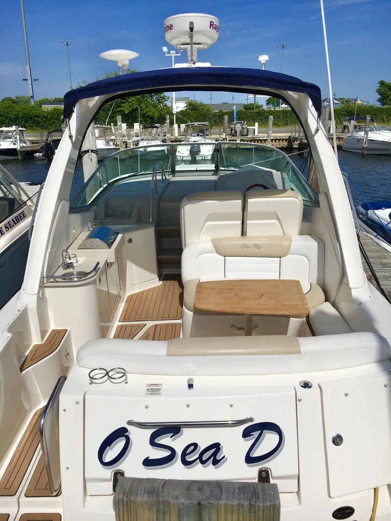 The Image of 2010 Sea Ray 330 Sundancer yacht docked, featuring spacious seating and a wooden table. - 0