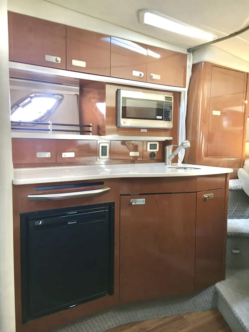Slide: The Image of 2010 Sea Ray 330 Sundancer interior kitchen with microwave, sink, and storage cabinets. - 23
