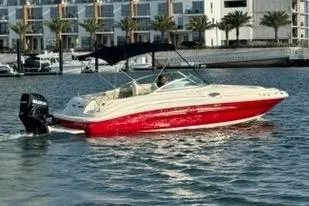 The Image of 2007 Sea Ray 240 Sundeck boat with red hull cruising near waterfront buildings. - 0