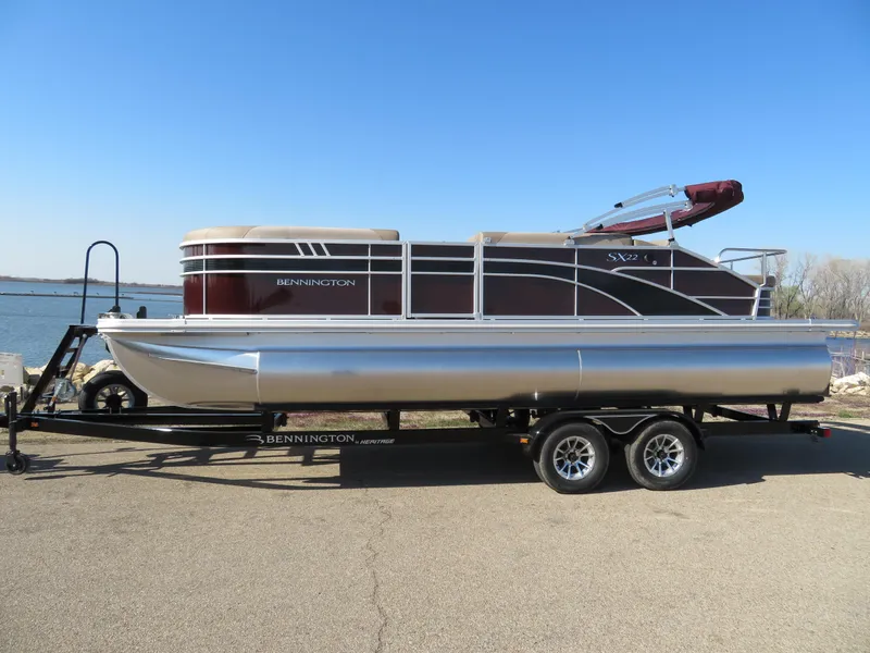 Slide: The Image of 2024 Bennington 22SXSB pontoon boat on a trailer by the water. - 0