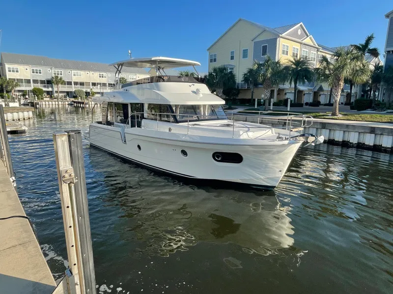 Slide: The Image of 2025 Beneteau Swift Trawler 48 docked in a marina with waterfront homes. - 2