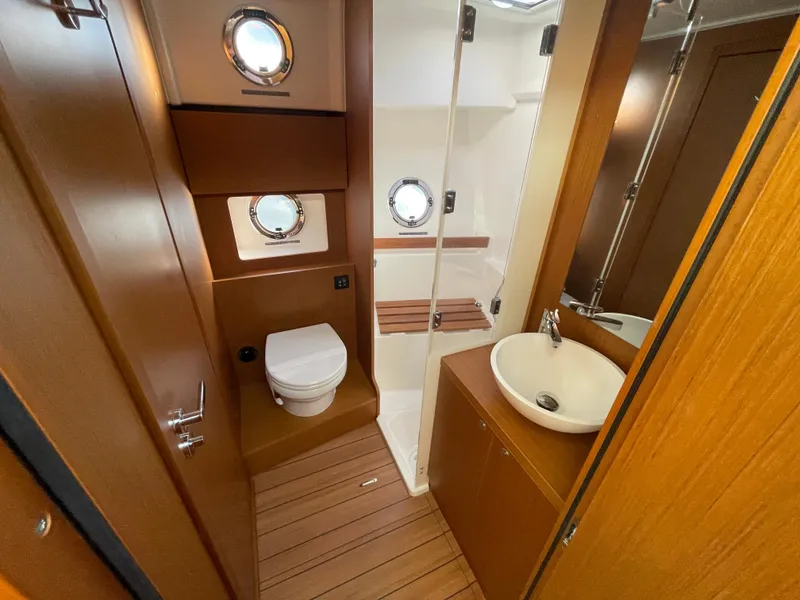 Slide: The Image of 2025 Beneteau Swift Trawler 48 bathroom with wooden finishes and porthole windows. - 44