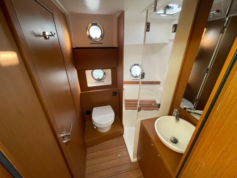 Slide: The Image of 2025 Beneteau Swift Trawler 48 bathroom with wooden finishes, porthole windows, toilet, sink, and shower. - 45