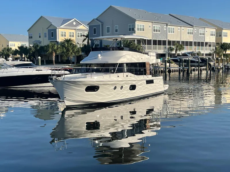 Slide: The Image of 2025 Beneteau Swift Trawler 48 docked in a marina with waterfront homes. - 5