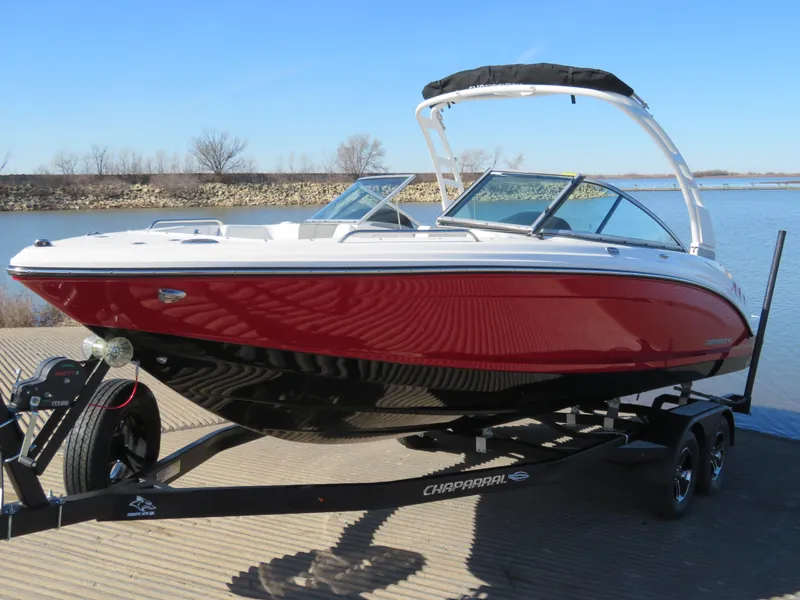 Slide: The Image of 2024 Chaparral 23 Surf boat with red and black hull on trailer by the lake. - 1