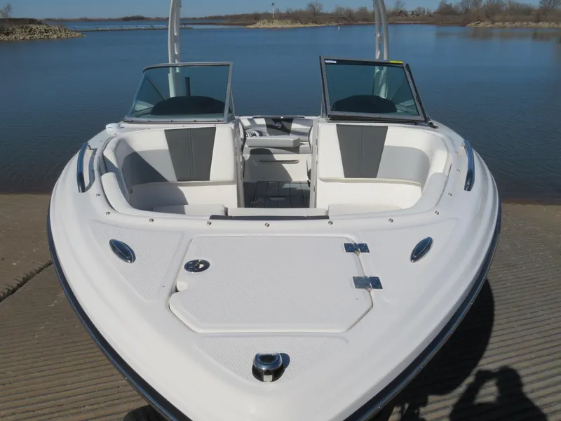 Slide: The Image of 2024 Chaparral 23 Surf boat with open bow seating, docked by a serene lake. - 4
