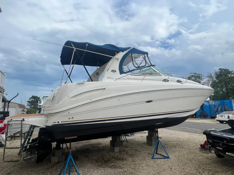 The Image of 2002 Sea Ray 300 Sundancer boat on stands, blue canopy, outdoor storage. - 0