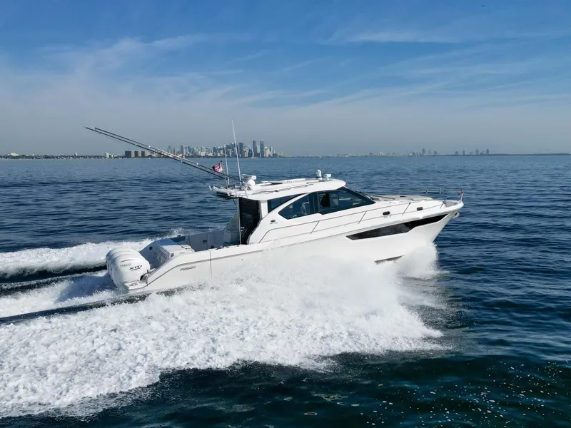 Slide: The Image of 2024 Pursuit OS 445 Offshore boat cruising on open water with city skyline in background. - 14