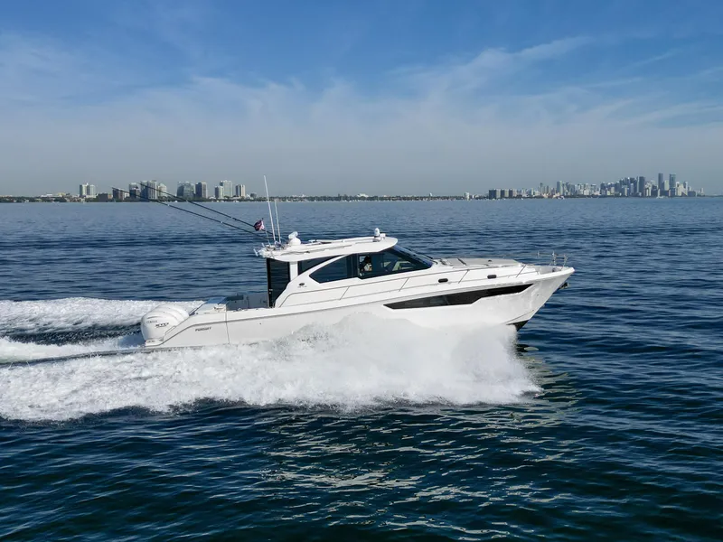 Slide: The Image of 2024 Pursuit OS 445 Offshore cruising on open water with city skyline in background. - 6