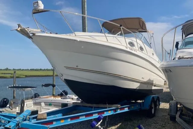The Image of 2004 Larson 240 Cabrio boat on trailer by the water, under a clear blue sky. - 1