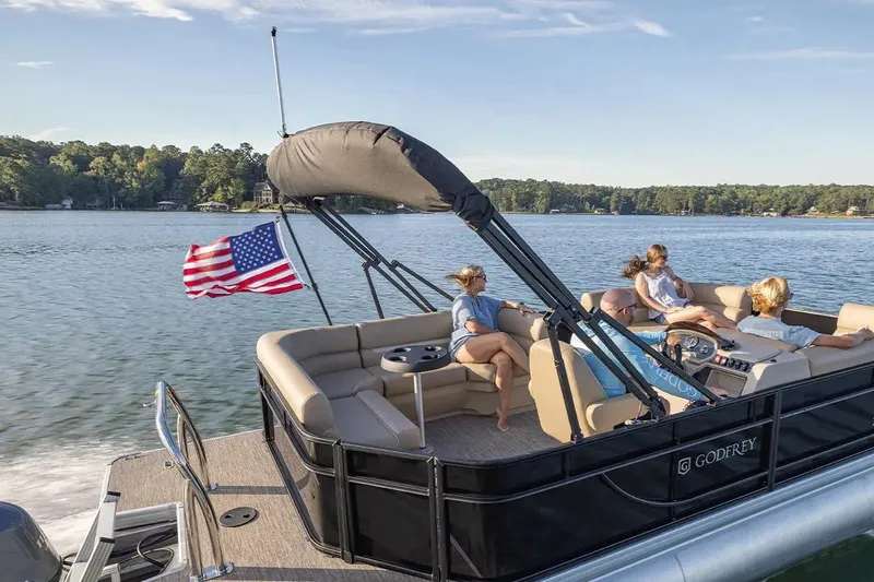 Slide: The Image of 2024 Sweetwater 2086 CX pontoon boat on a lake, with passengers relaxing under a canopy. - 8