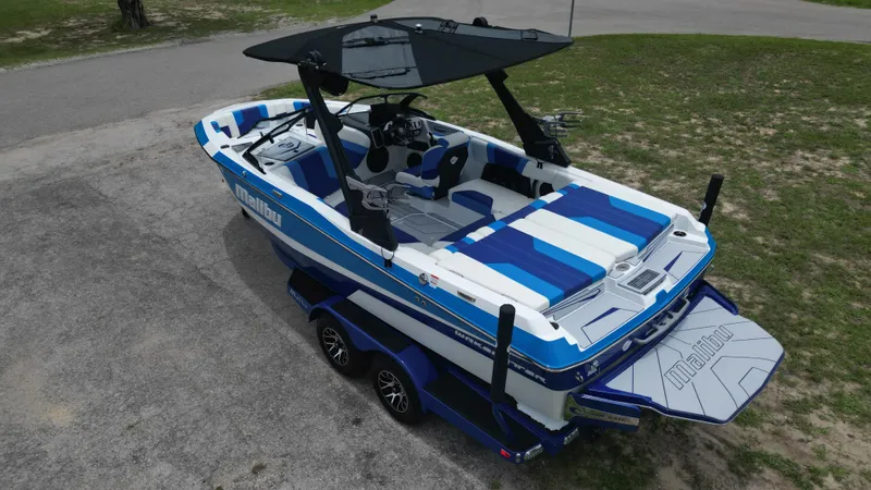 Slide: The Image of 2024 Malibu Wakesetter 21 LX boat with blue and white interior, parked on a trailer. - 10