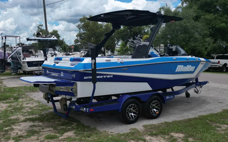 Slide: The Image of 2024 Malibu Wakesetter 21 LX boat on a trailer in a marina. - 2
