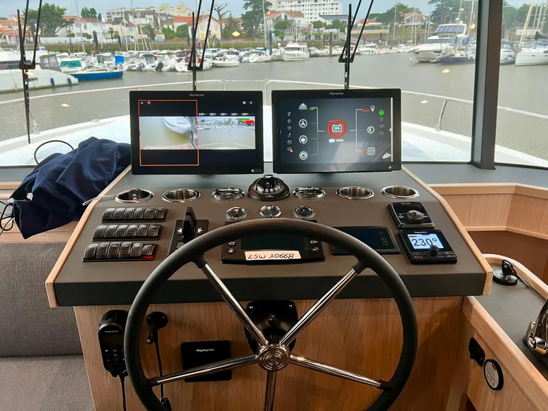 Slide: The Image of Beneteau Swift Trawler 54 2025 helm station with dual navigation screens and marina view. - 2