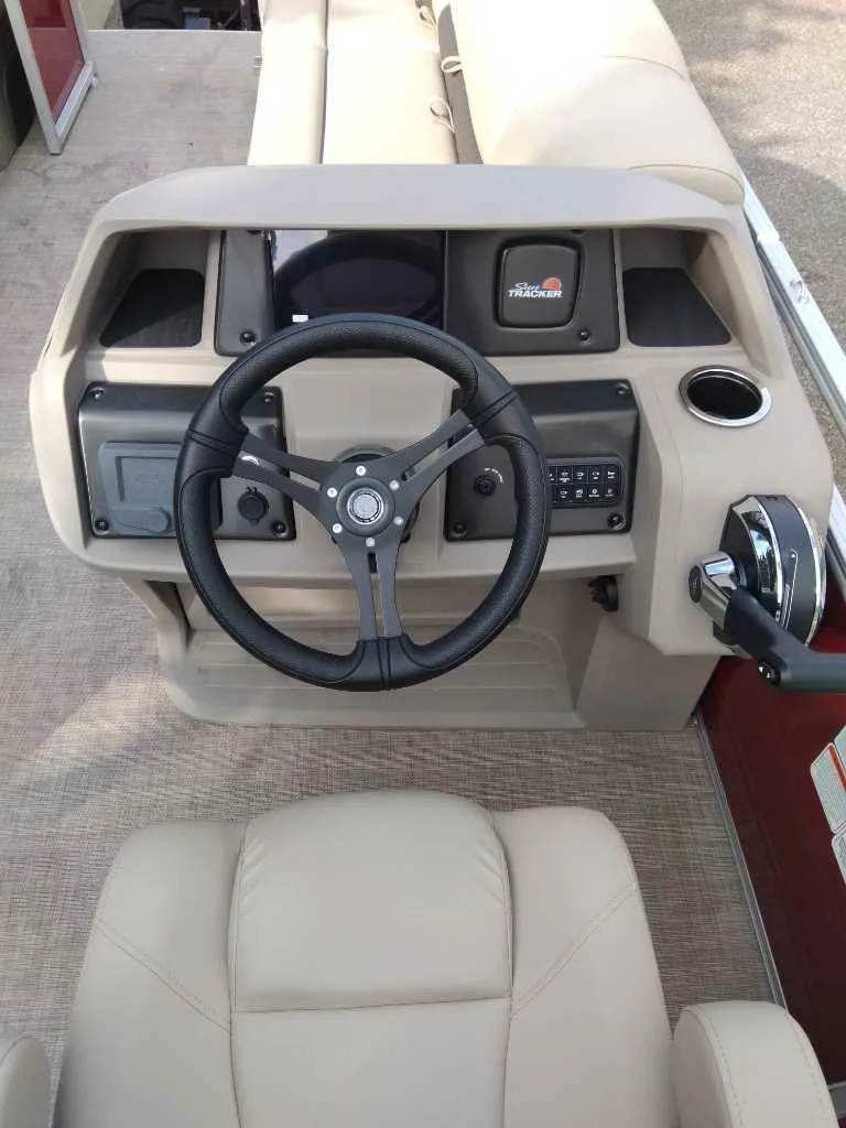 Slide: The Image of 2024 Sun Tracker Party Barge 20 DLX steering console with beige seating and controls. - 6