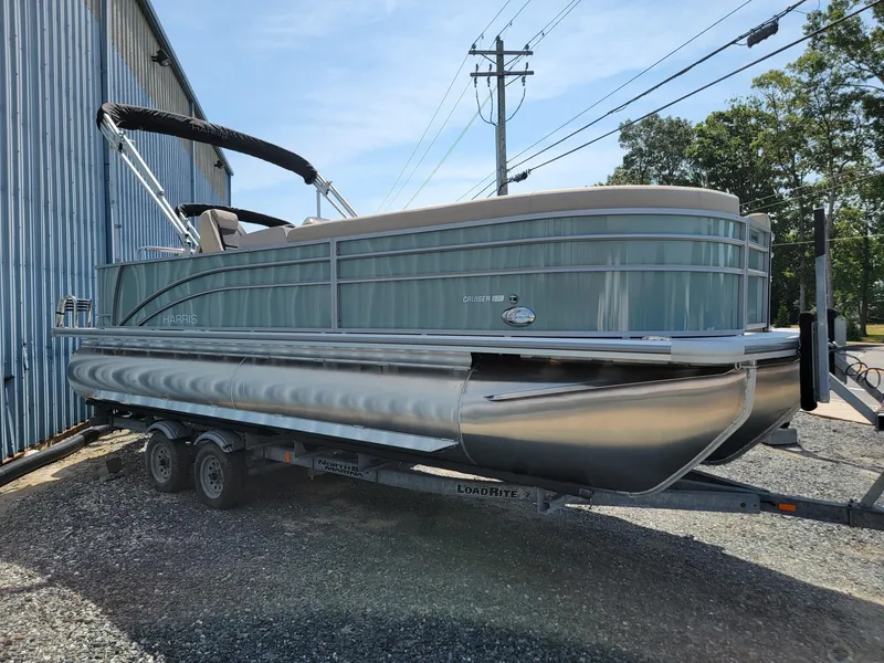 Slide: The Image of 2025 Harris Cruiser 230 pontoon boat on a trailer outside a metal building. - 2