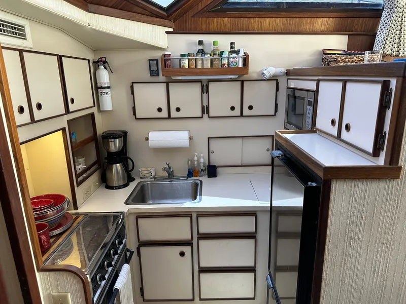 Slide: The Image of Compact kitchen area in a 1985 Hatteras 36 Convertible yacht with white cabinets and appliances. - 17