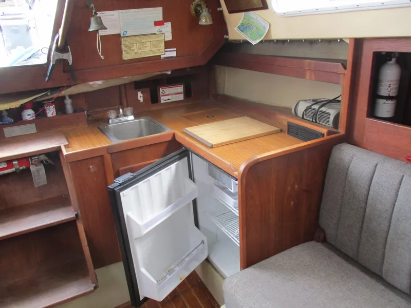 Slide: The Image of 1979 CAL 31 sailboat interior with kitchenette, featuring a sink, fridge, and wooden cabinetry. - 24