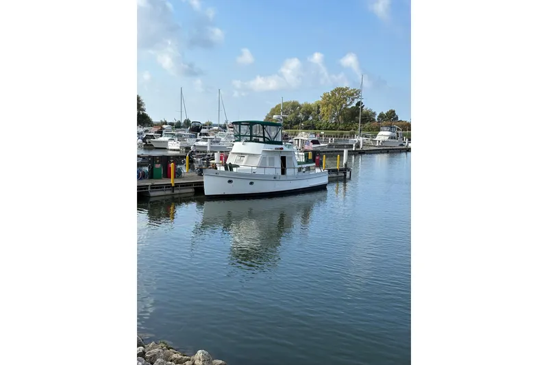 Slide: The Image of 1982 Monk 40 boat docked at a marina, surrounded by calm water and other vessels. - 34