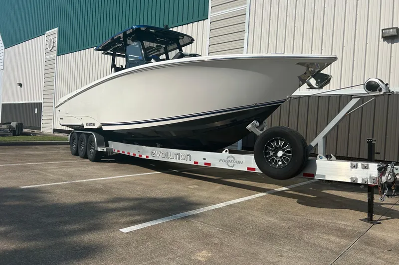 The Image of 2025 Fountain 32 NX boat on trailer, parked outside a large building. - 0