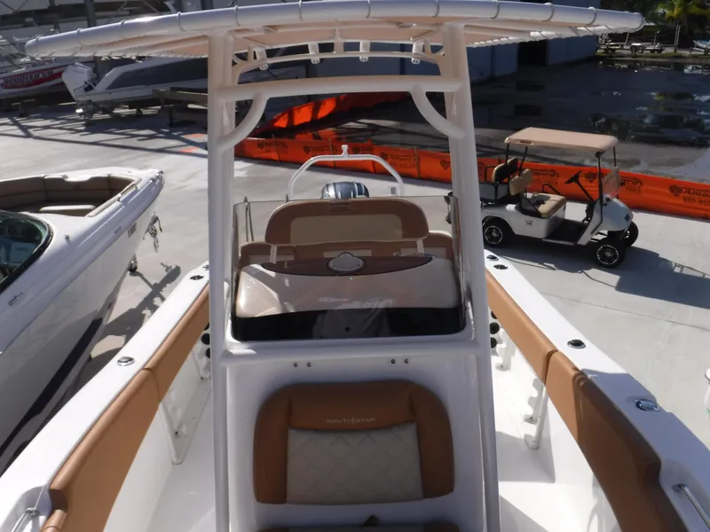 Slide: The Image of 2024 NauticStar 212 Legacy boat with tan seating and T-top, docked near other boats. - 5