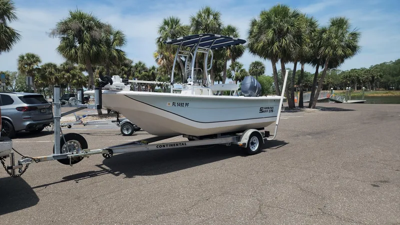 Slide: The Image of 2011 Carolina Skiff 178 DLV boat on trailer, parked near palm trees. - 13
