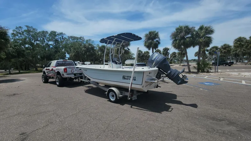 Slide: The Image of 2011 Carolina Skiff 178 DLV boat on trailer, parked near palm trees under a blue sky. - 14