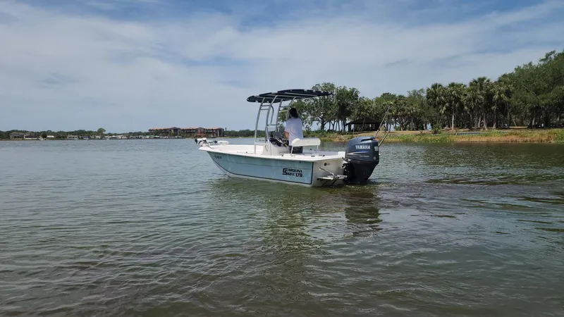 Slide: The Image of 2011 Carolina Skiff 178 DLV boat on calm water near a tree-lined shore. - 48
