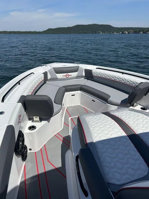 Slide: The Image of 2024 Fountain 32 NX boat interior with seating, on a lake with hills in the background. - 6