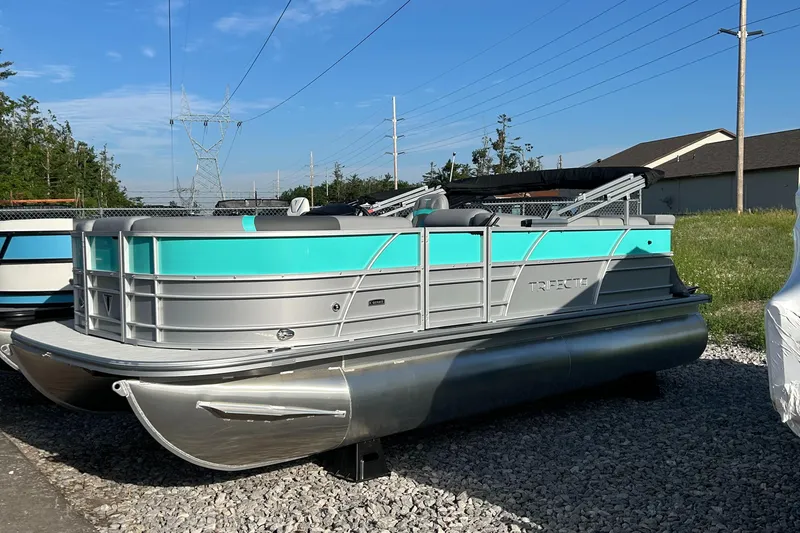 The Image of 2025 Trifecta 20CCS pontoon boat with teal and silver design, parked on gravel. - 0