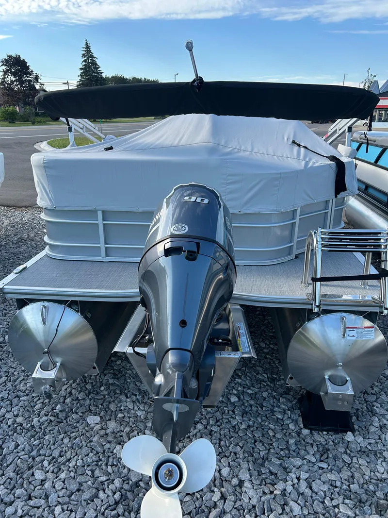 Slide: The Image of 2025 Trifecta 20CCS pontoon boat with outboard motor, covered and parked on gravel. - 5
