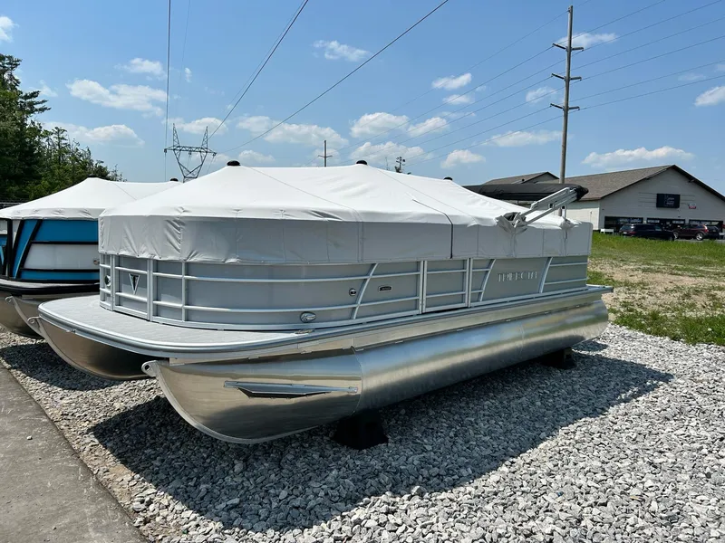 Slide: The Image of 2025 Trifecta 20CCS pontoon boat with cover, parked on gravel lot under blue sky. - 8