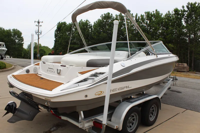 Slide: The Image of 2011 Regal 2100 boat on trailer, parked outdoors, featuring sleek design and spacious seating. - 7